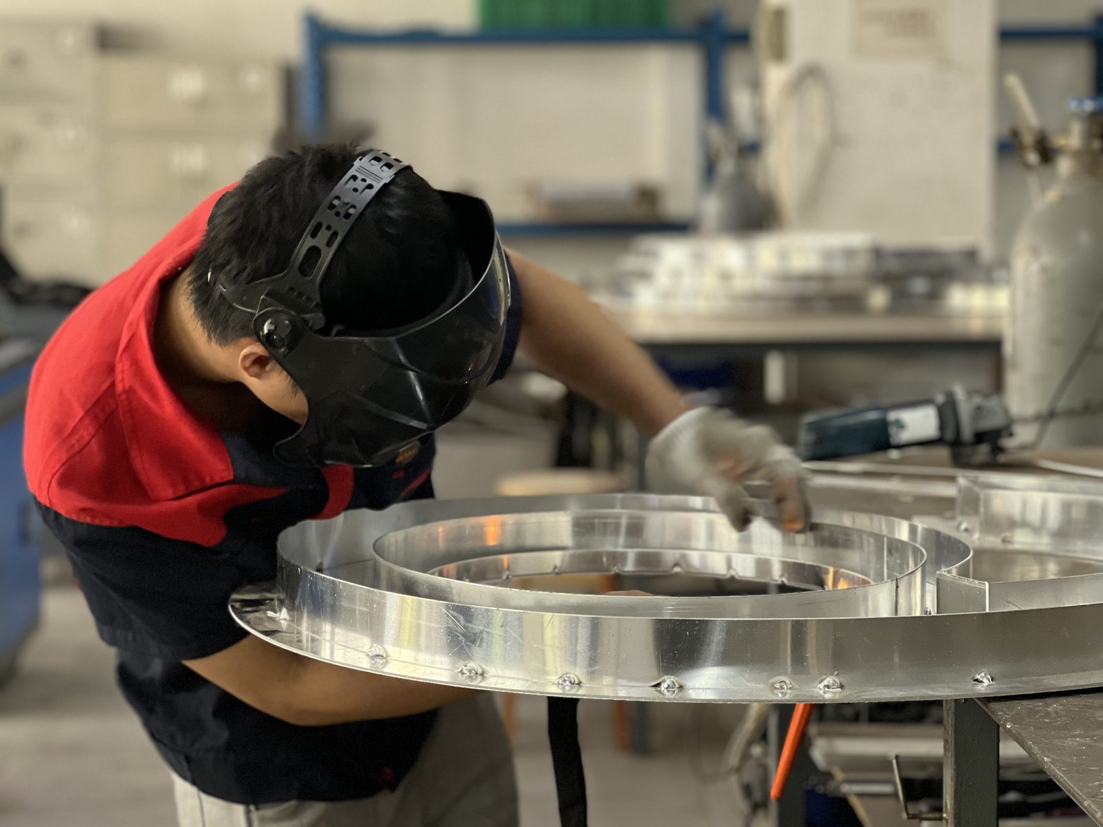 Welder assembling a large stainless steel ring letter